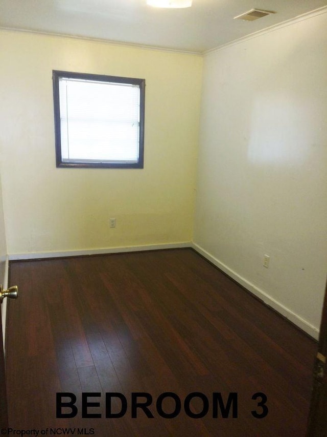 empty room with dark hardwood / wood-style flooring and crown molding