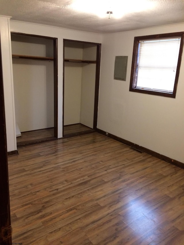 unfurnished bedroom with two closets, dark wood-type flooring, electric panel, and a textured ceiling