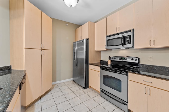 kitchen featuring stainless steel appliances, light tile patterned floors, light brown cabinetry, and dark stone counters