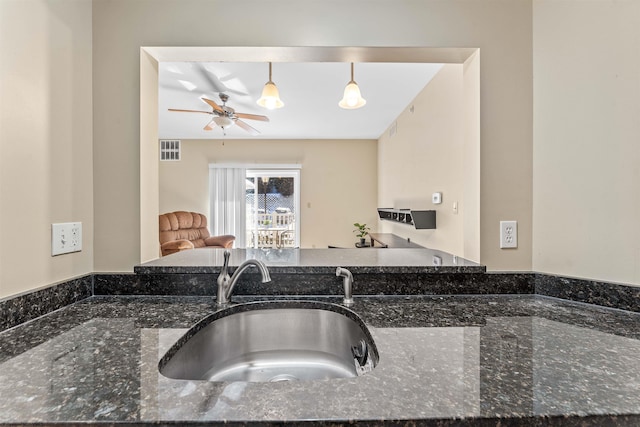 kitchen with ceiling fan, decorative light fixtures, sink, and dark stone countertops