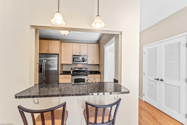 kitchen featuring appliances with stainless steel finishes, dark stone countertops, hanging light fixtures, kitchen peninsula, and light brown cabinets