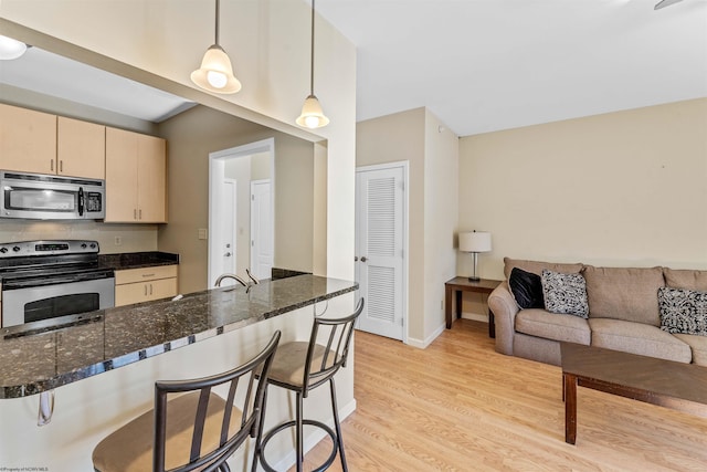 kitchen featuring stainless steel appliances, a breakfast bar area, pendant lighting, and dark stone counters