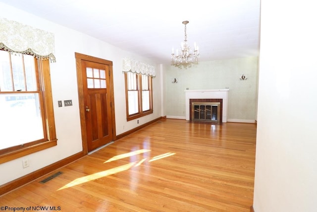 unfurnished living room with a brick fireplace, hardwood / wood-style floors, and an inviting chandelier