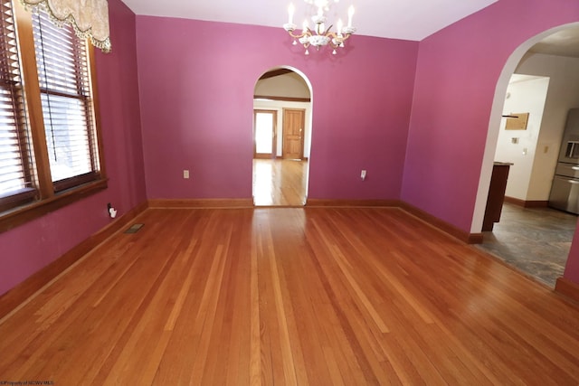 unfurnished room featuring hardwood / wood-style flooring, plenty of natural light, and an inviting chandelier