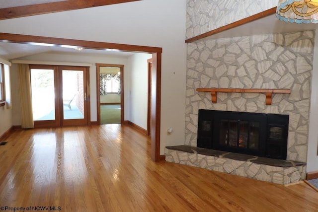 unfurnished living room featuring hardwood / wood-style floors, a fireplace, vaulted ceiling with beams, and french doors