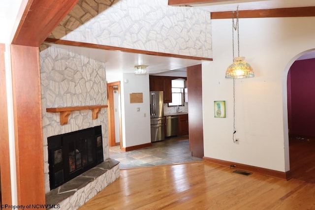 unfurnished living room with beam ceiling, sink, a stone fireplace, and wood-type flooring