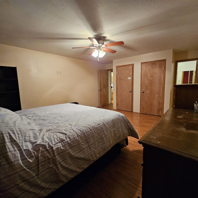 bedroom featuring multiple closets, a textured ceiling, hardwood / wood-style floors, and ceiling fan