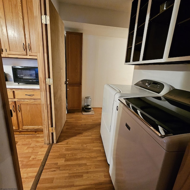 clothes washing area featuring cabinets, washing machine and clothes dryer, and light hardwood / wood-style floors