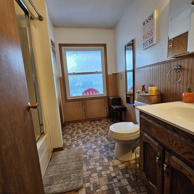 full bathroom with vanity, toilet, combined bath / shower with glass door, and wood walls