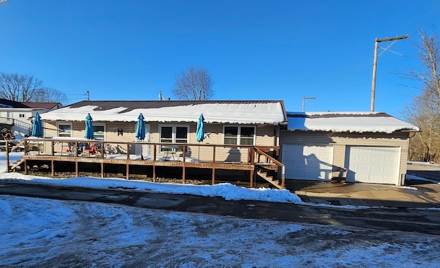 snow covered back of property with a garage and a deck