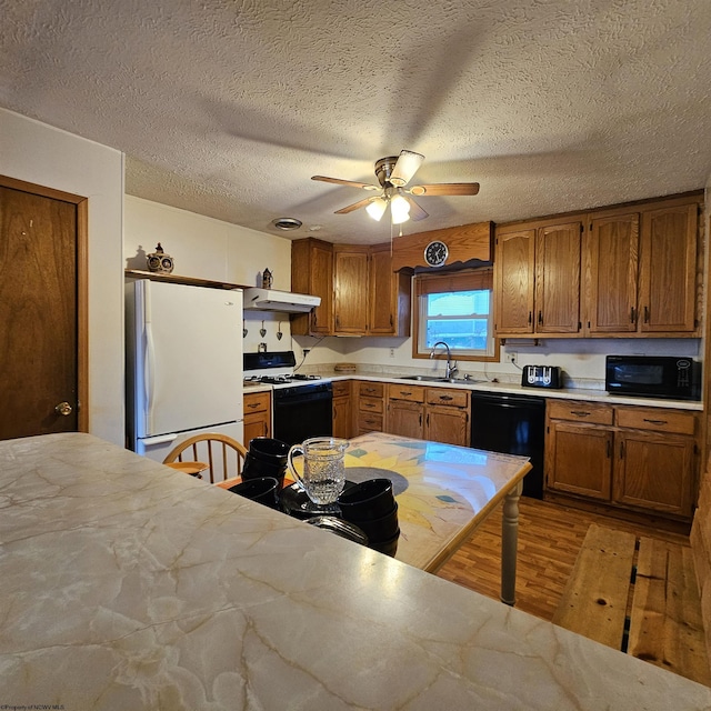 kitchen featuring sink, light wood-type flooring, ceiling fan, black appliances, and a textured ceiling