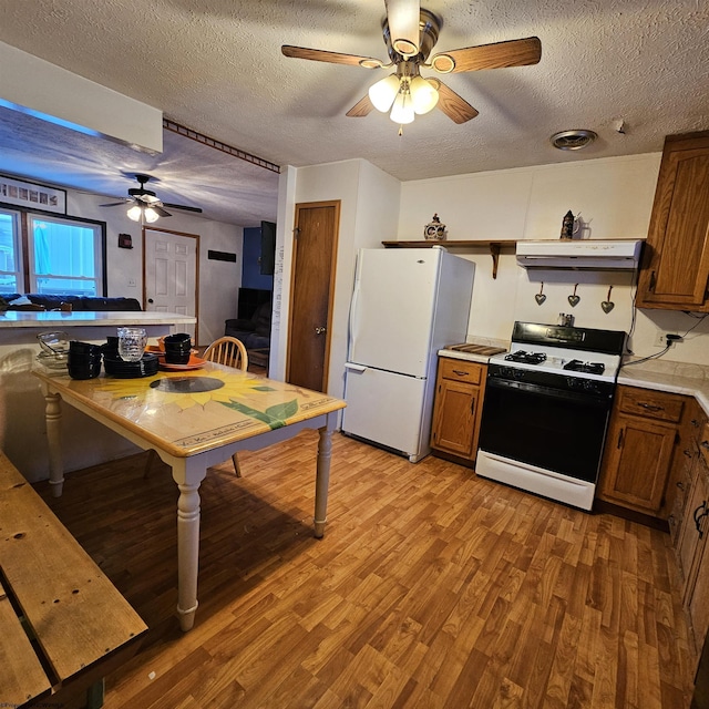 kitchen with light hardwood / wood-style flooring, range with gas stovetop, a textured ceiling, and white fridge