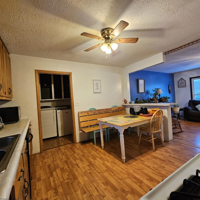 dining space with ceiling fan, light hardwood / wood-style flooring, washer and dryer, and a textured ceiling