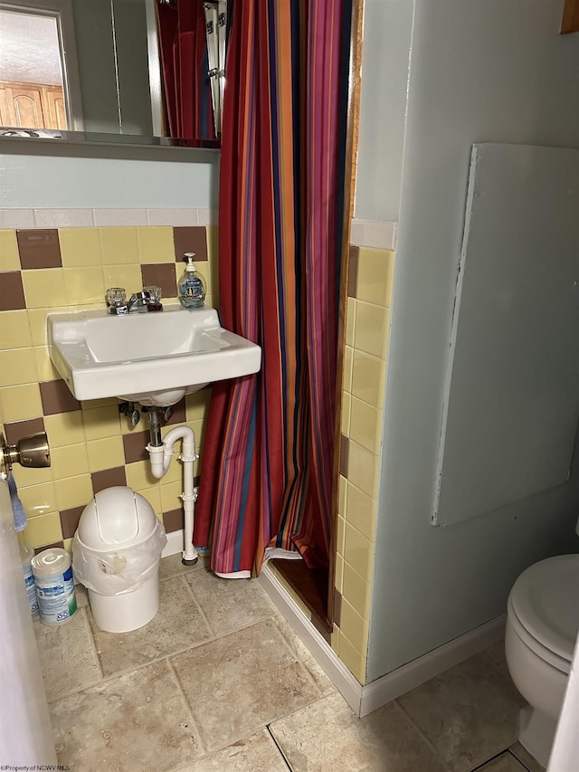 bathroom with toilet, sink, and tile walls