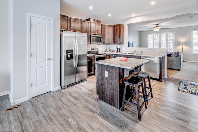 kitchen featuring a kitchen island, appliances with stainless steel finishes, a breakfast bar, sink, and light wood-type flooring