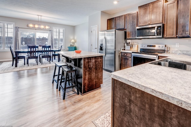 kitchen with pendant lighting, stainless steel appliances, a center island, a wealth of natural light, and a kitchen bar