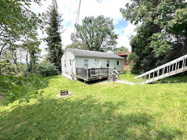 back of property featuring a wooden deck, a lawn, and a fire pit