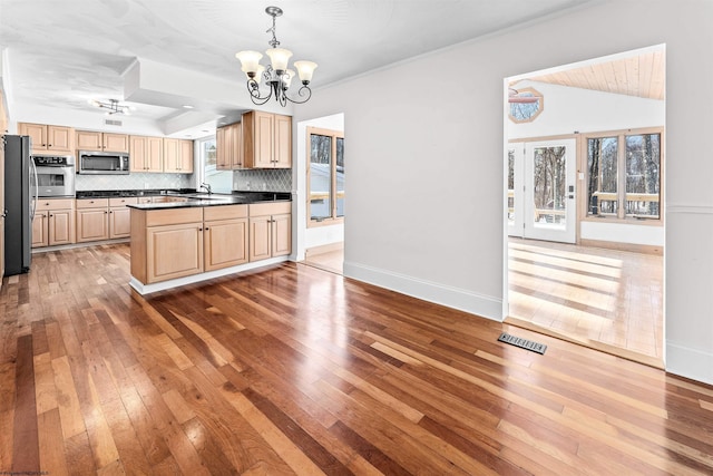 kitchen with backsplash, stainless steel appliances, light brown cabinets, decorative light fixtures, and light wood-type flooring