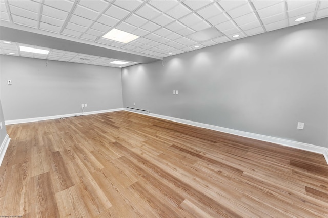 unfurnished room featuring a baseboard heating unit, a drop ceiling, and light wood-type flooring