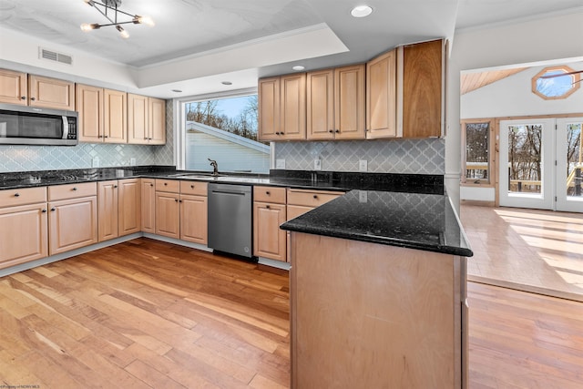 kitchen with light brown cabinetry, crown molding, dark stone counters, light wood-type flooring, and stainless steel appliances