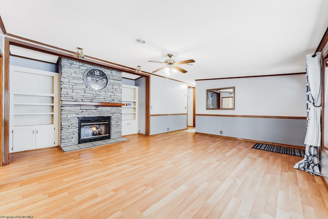 unfurnished living room with ceiling fan, a fireplace, ornamental molding, light hardwood / wood-style floors, and built in shelves