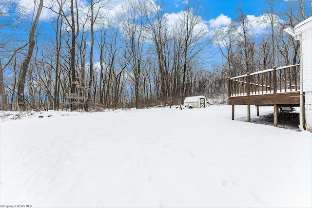 yard covered in snow featuring a storage shed and a deck