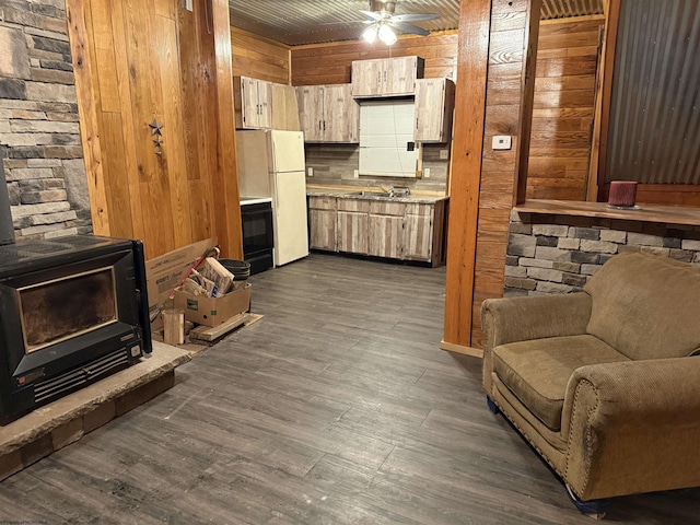 living room with sink, dark wood-type flooring, ceiling fan, wooden walls, and a wood stove