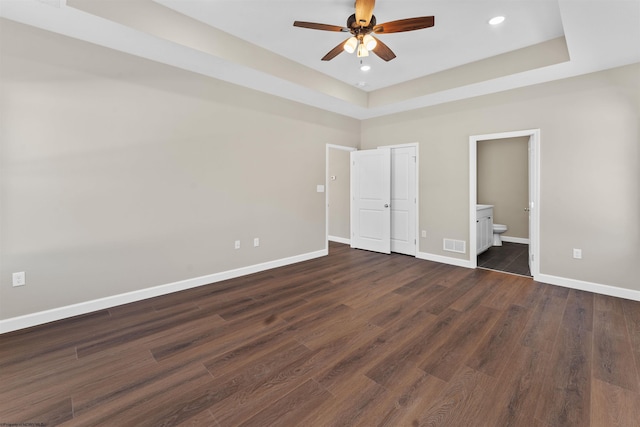 unfurnished bedroom with a raised ceiling, ceiling fan, dark hardwood / wood-style floors, and ensuite bath