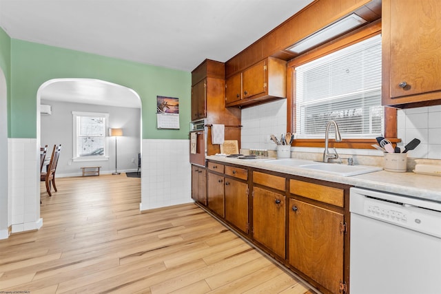 kitchen featuring sink, tasteful backsplash, light wood-type flooring, white dishwasher, and oven