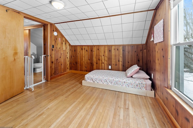 bedroom featuring ensuite bathroom, lofted ceiling, light hardwood / wood-style floors, and wood walls