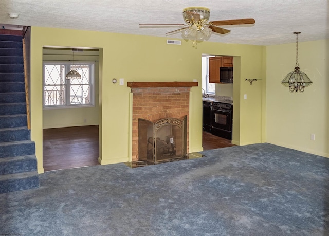 unfurnished living room with a brick fireplace, ceiling fan, a textured ceiling, and dark colored carpet