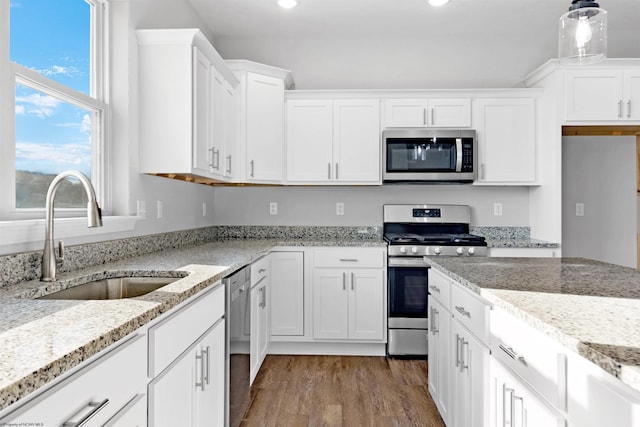 kitchen with sink, hanging light fixtures, stainless steel appliances, light stone countertops, and white cabinets