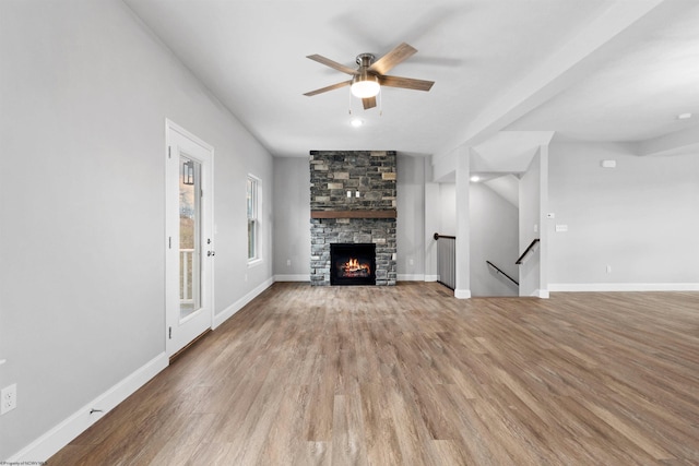 unfurnished living room featuring ceiling fan, a stone fireplace, and hardwood / wood-style floors