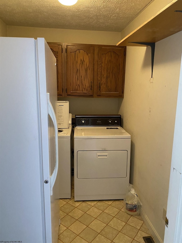 laundry room with cabinets, light tile patterned floors, washer and dryer, and a textured ceiling