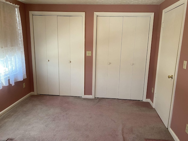 unfurnished bedroom featuring light colored carpet and multiple closets