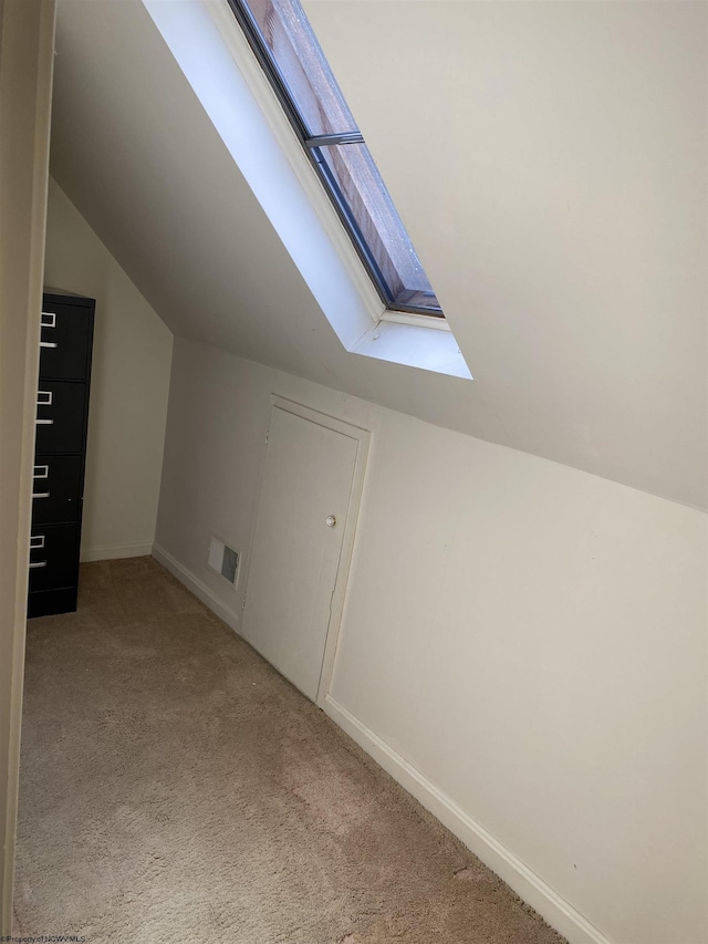 additional living space featuring vaulted ceiling with skylight and light carpet