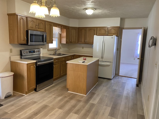 kitchen featuring appliances with stainless steel finishes, sink, hanging light fixtures, a center island, and light hardwood / wood-style floors