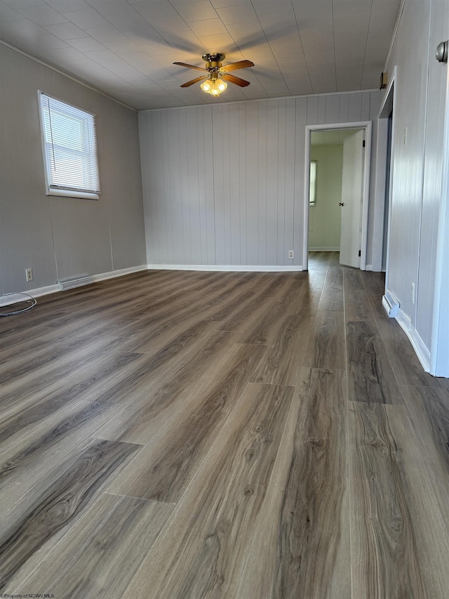 spare room with dark wood-type flooring, wooden walls, and ceiling fan