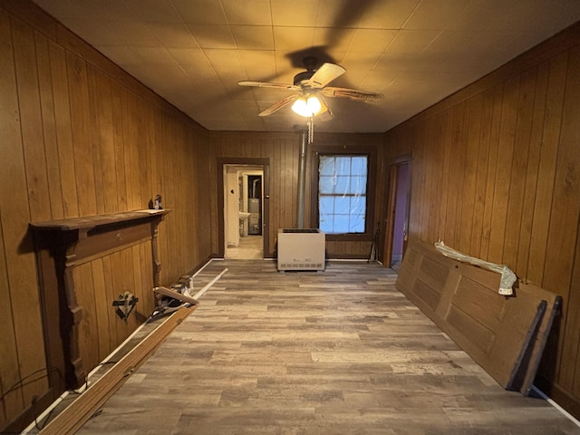 interior space featuring ceiling fan, heating unit, wooden walls, and light hardwood / wood-style flooring