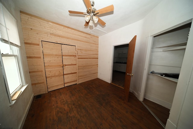 unfurnished bedroom with dark hardwood / wood-style flooring, a closet, ceiling fan, and wood walls