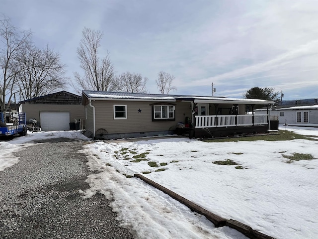 view of front facade with driveway, a detached garage, metal roof, an outbuilding, and a porch