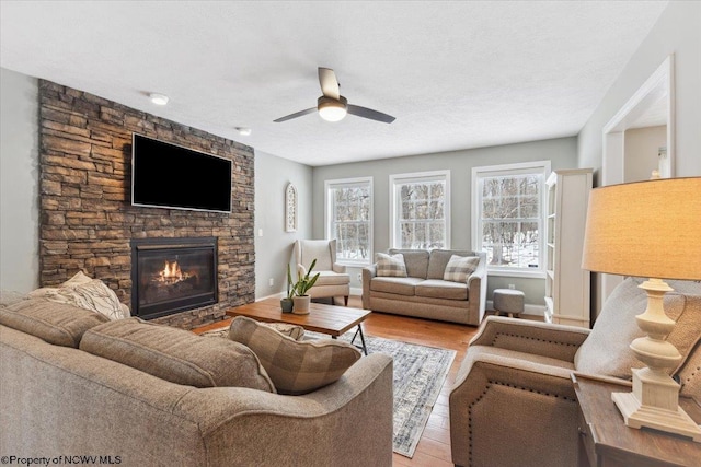 living room with light hardwood / wood-style flooring, ceiling fan, a fireplace, and a textured ceiling