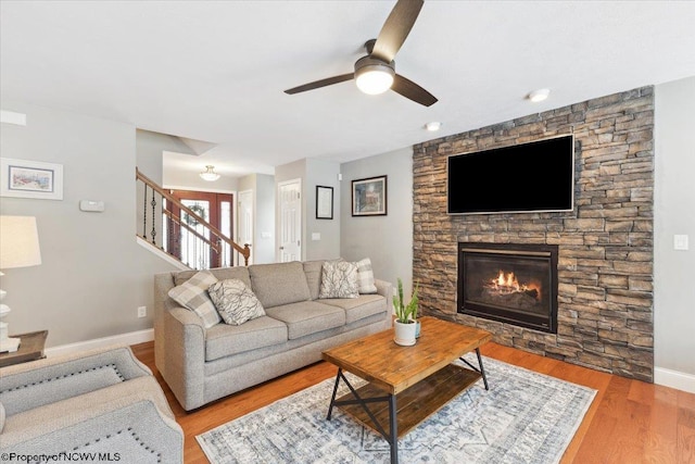 living room featuring ceiling fan, a fireplace, and light wood-type flooring