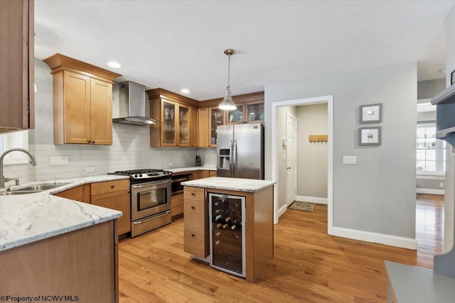 kitchen with appliances with stainless steel finishes, pendant lighting, sink, beverage cooler, and wall chimney range hood