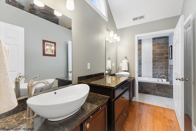 bathroom featuring hardwood / wood-style flooring, vanity, lofted ceiling, and a relaxing tiled tub