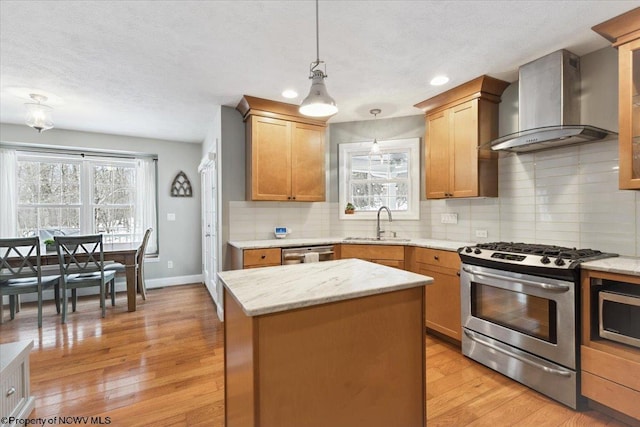 kitchen with a kitchen island, appliances with stainless steel finishes, pendant lighting, sink, and wall chimney range hood