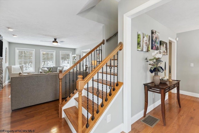 stairway with hardwood / wood-style floors and ceiling fan