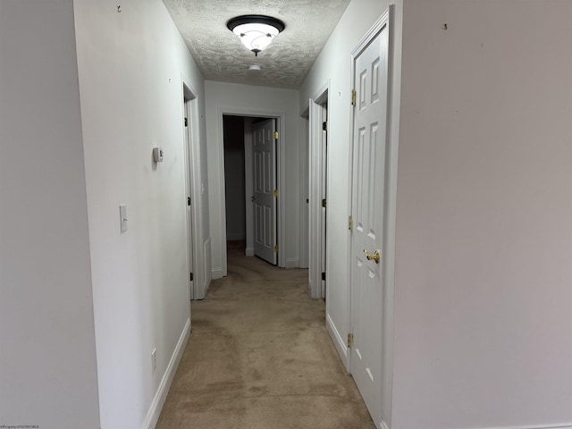 hall with light colored carpet and a textured ceiling