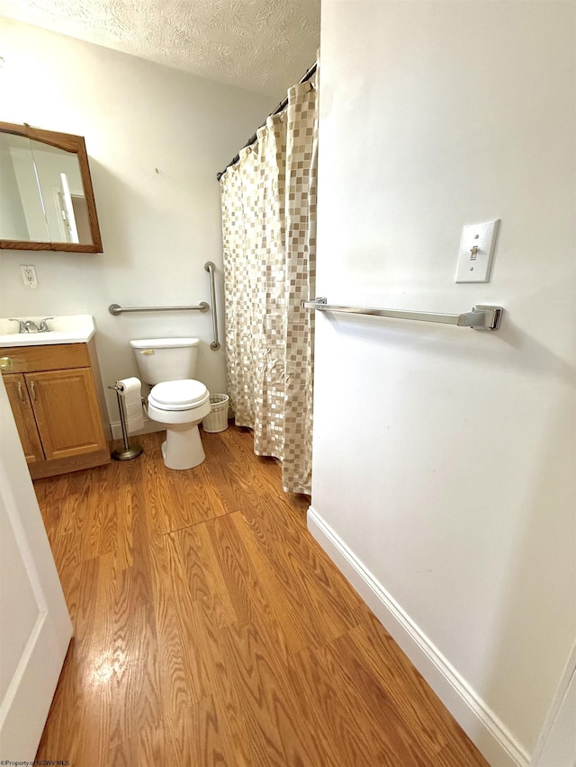 bathroom featuring wood-type flooring, toilet, a textured ceiling, and vanity