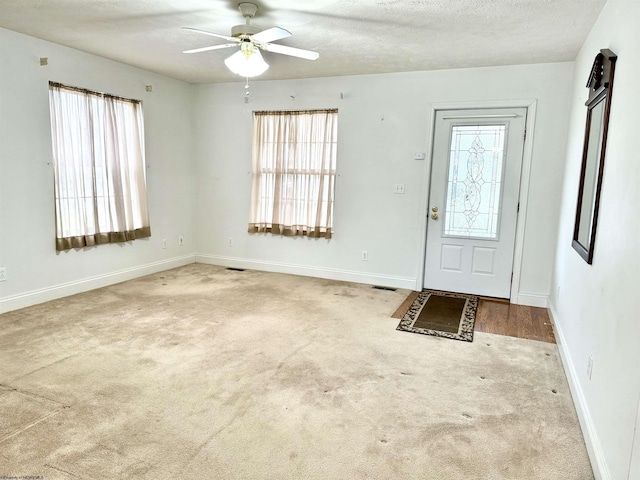 foyer entrance with ceiling fan, carpet floors, and a textured ceiling